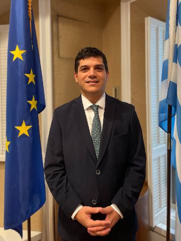 Emmanuel Koubarakis stands between two flags, one of which is the Greek flag and one is the European Union flag. Emmanuel Koubarakis