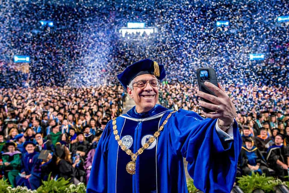 SLU President Fred Pestello takes a selfie on stage at the 2025 SLU Commencement ceremony