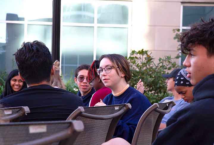 A group of students sit in chairs on an outside patio