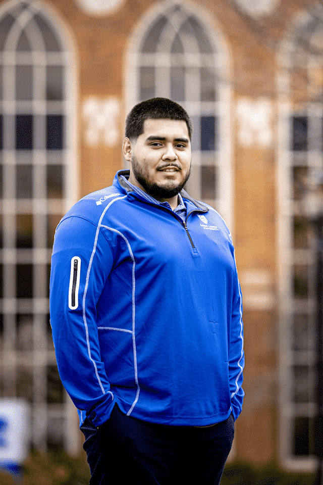 Gael Cosgaya poses for a photo outside of a brick building on campus.