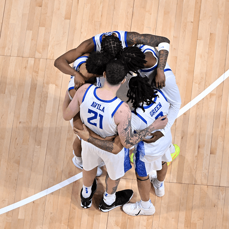 A group of basketball players forms a huddle on a backetball court.