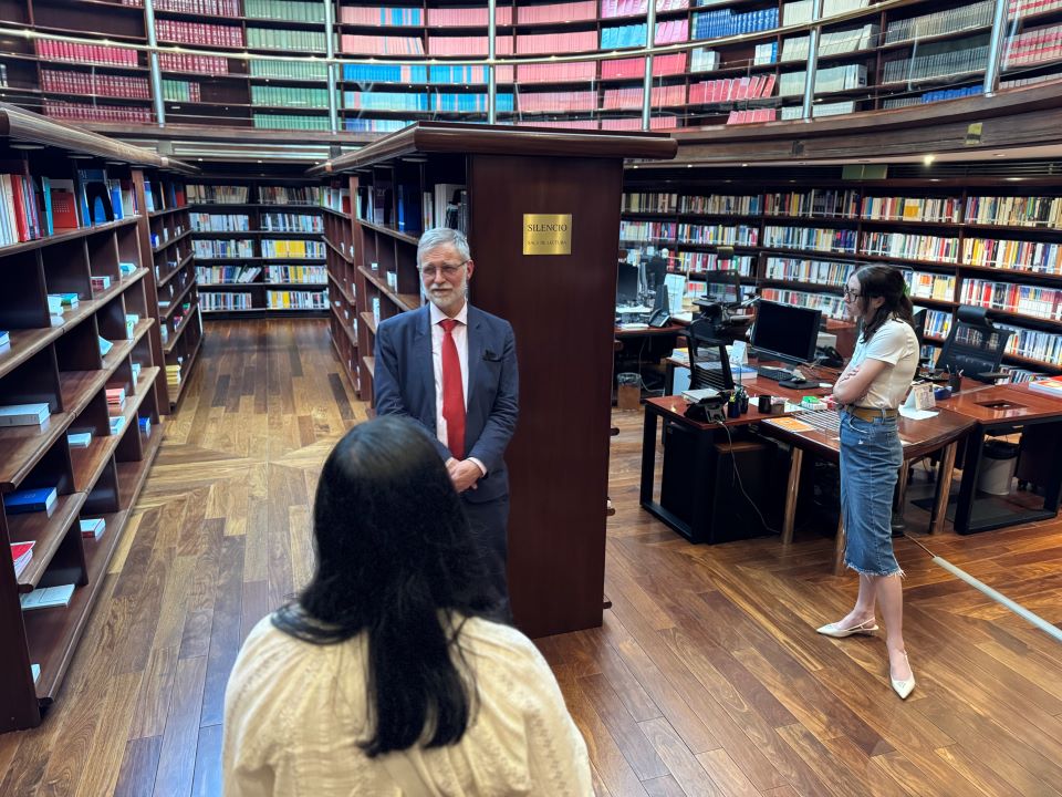 Students tour the library students and tour guide in a library surrounded by shelves of books and tables