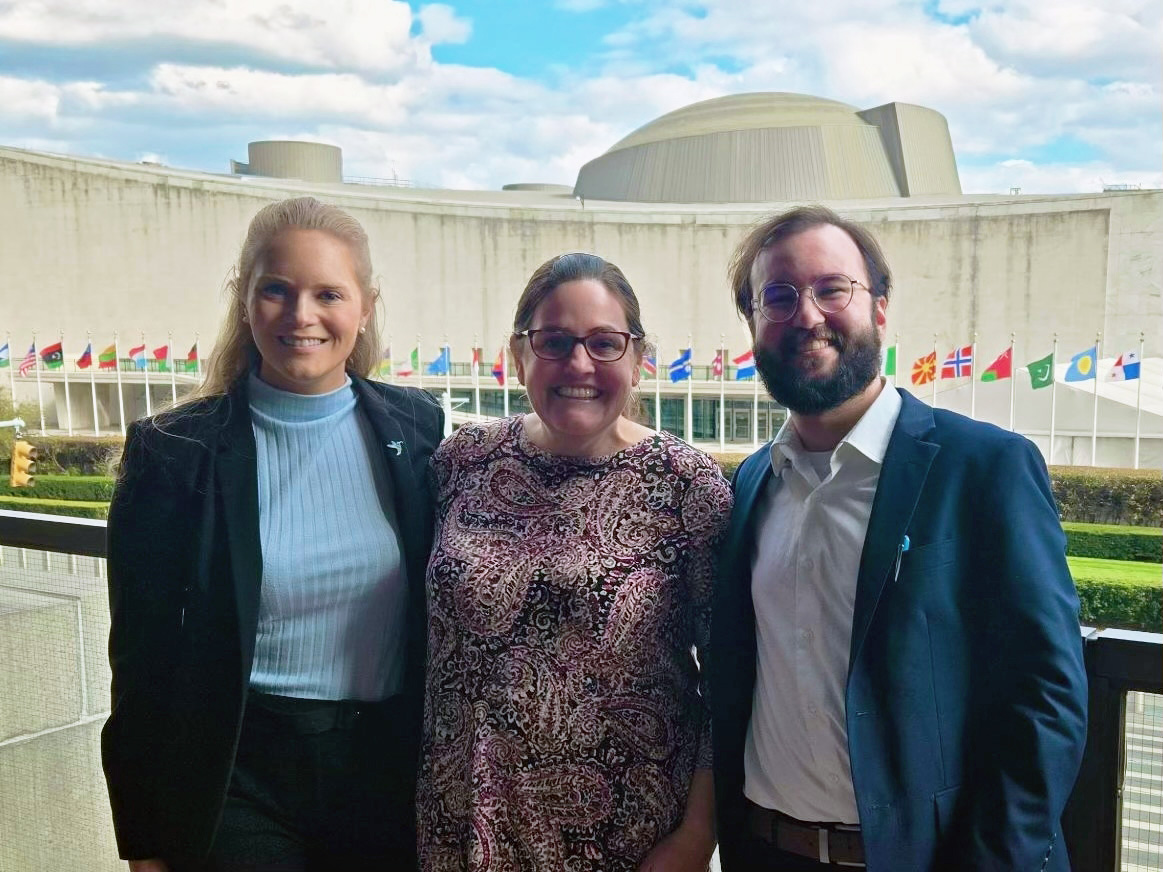 clinic students and professor in front of a building lined with flags.