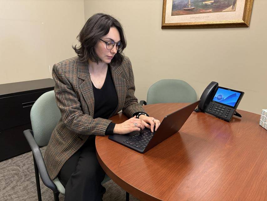 Clinic student Shannon Besch works on a laptop at a table in an office.