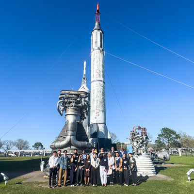 Students standing in front of a rocket outside of the NASA building.