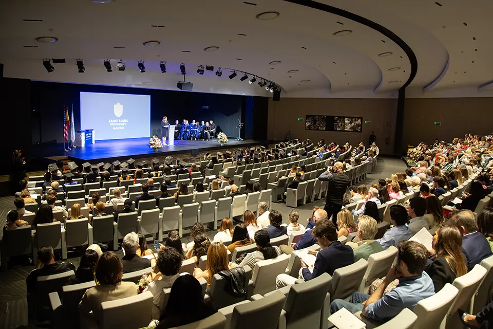 Woman on stages talks to auditorium full of people.