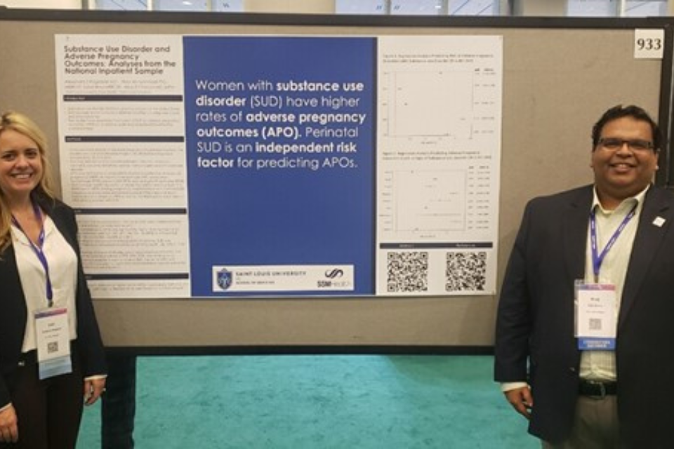 Two students stand in front of a research poster at an event.