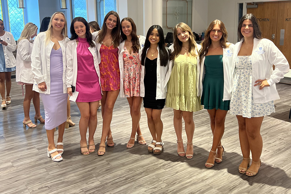 A group of female students pose for a photo in their white coats at a reception.