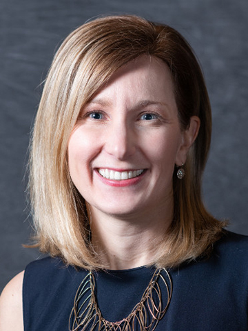 Laura Schrubb headshot, in black shirt with blonde hair and a grey backdrop.
