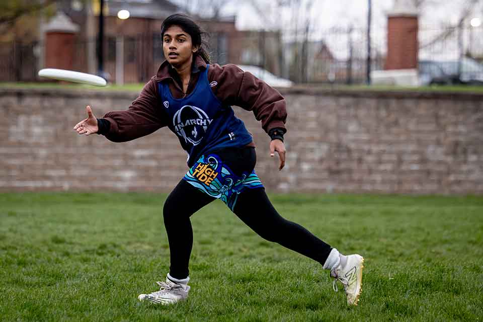 A female ultimate frisbee team member throws the frisbee while practicing on a green field.