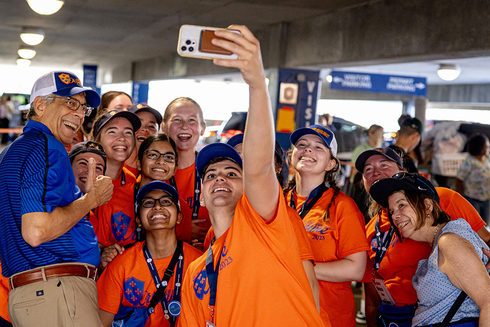 Pestello in a polo shirt and khakis poses for a selfie with numerous orange-shirted Oriflamme members in the Laclede Garage during Fall Welcome in 2023.