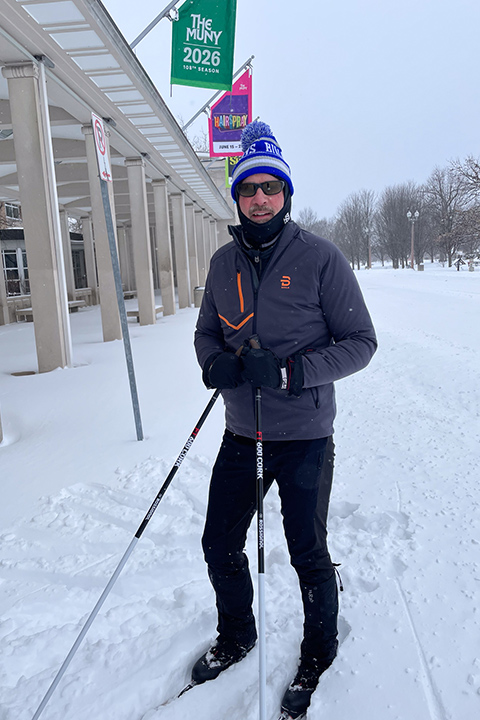 A tall white man in winter gear on cross-country skis, in an urban park